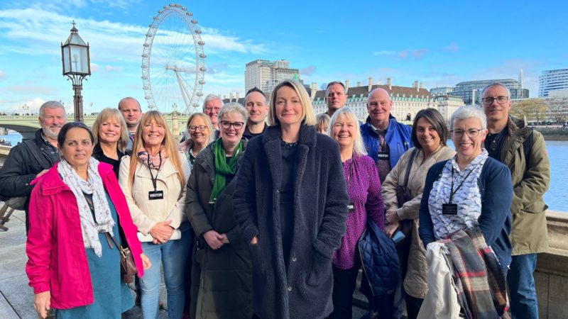 Jessica Morden MP stands on the terrace at the house of Commons with a number of constituents behind her on a bright, sunny day. 