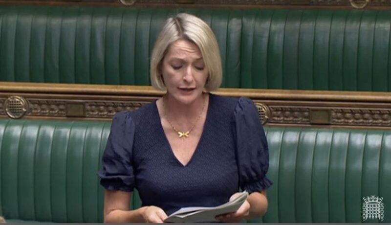 Jessica Morden stands in Parliament asking a question. The green benches are behind her. 